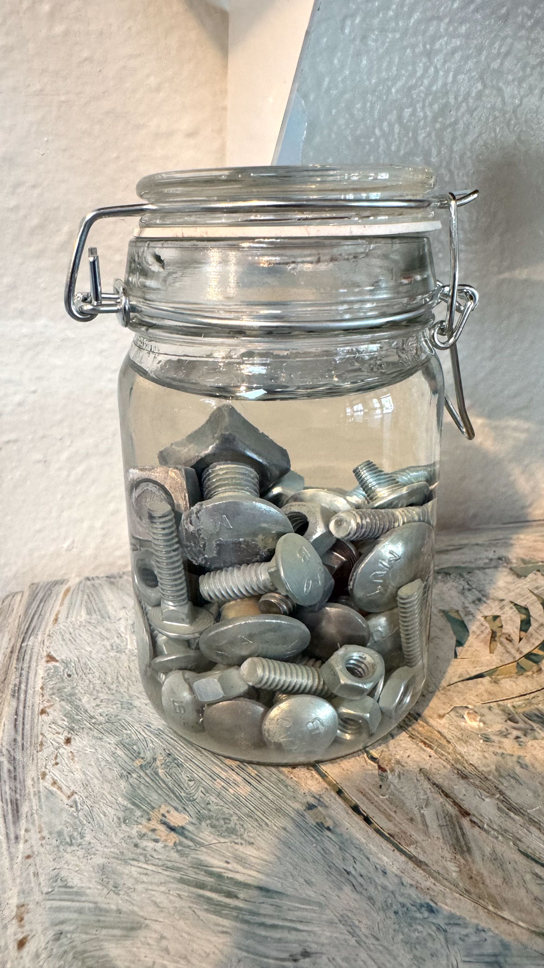 wall installation with glass jars containing harware, cutlery, yarn, fabric, collaged shelves
