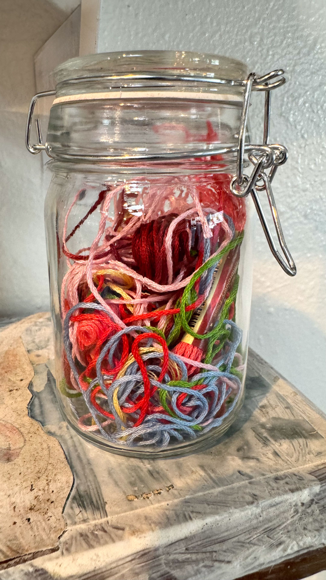 wall installation with glass jars containing harware, cutlery, yarn, fabric, collaged shelves