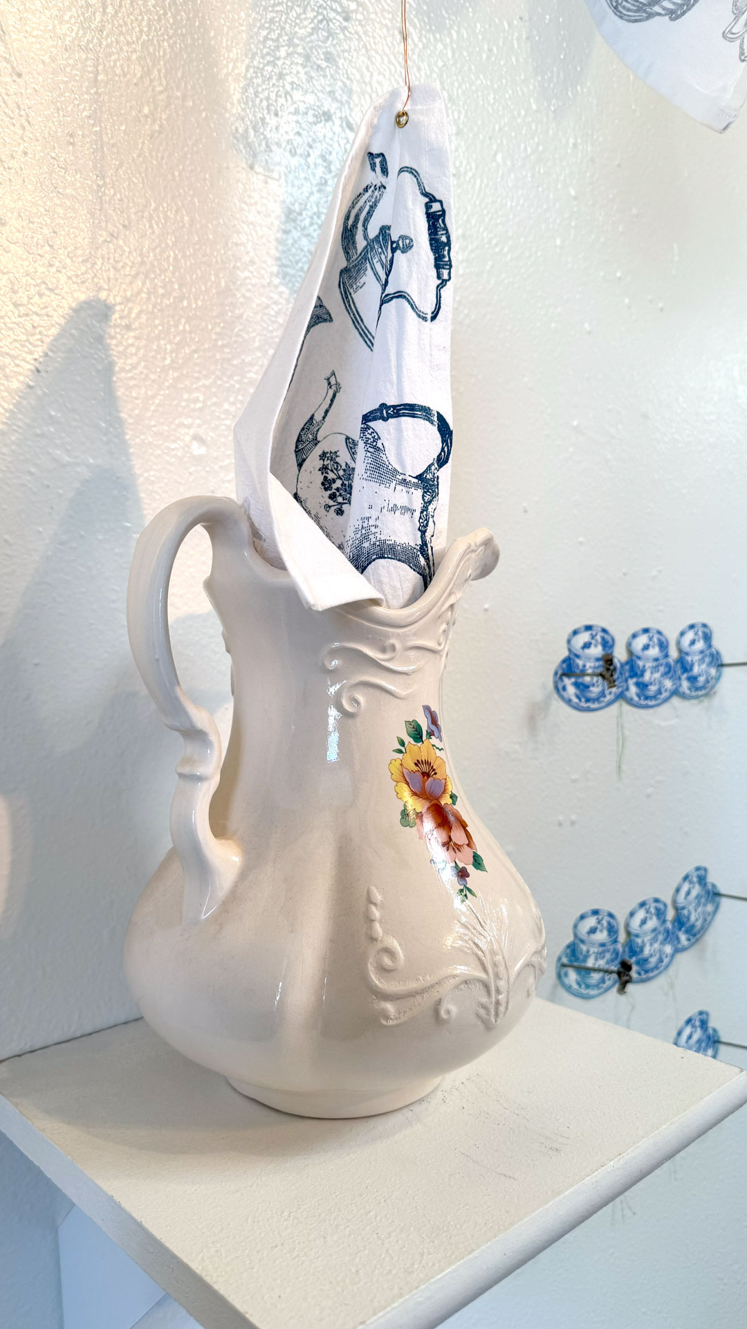installation with installation with silkscreen napkins attached to ceiling in an arch travelling from a box to a pitcher