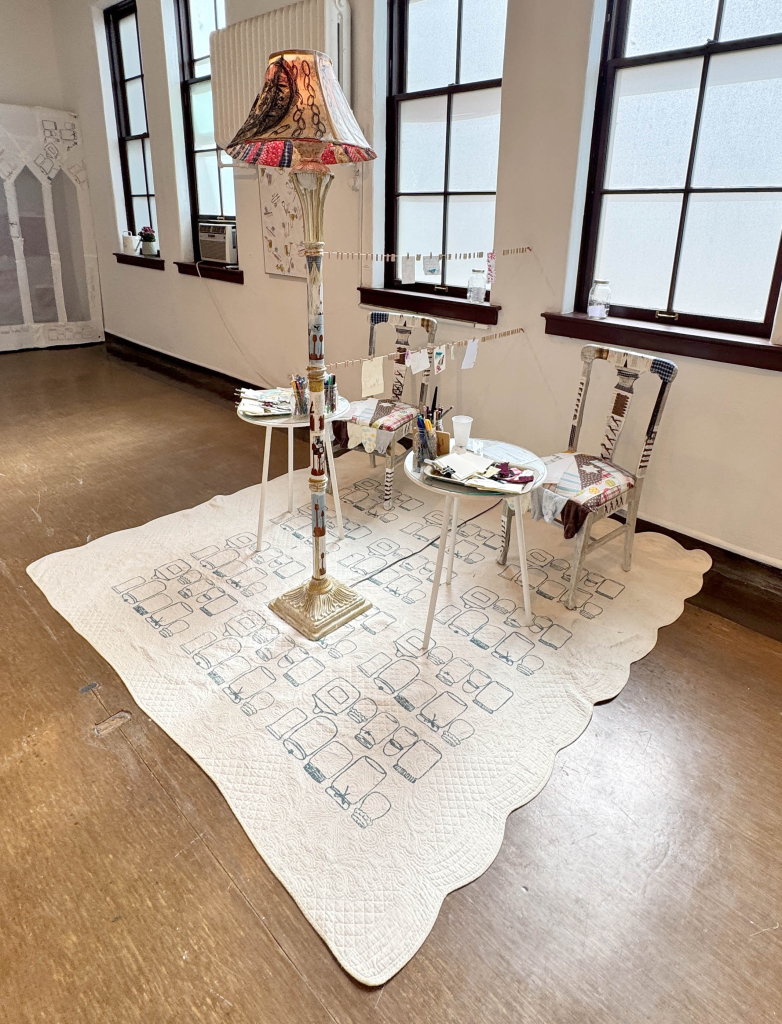installation with two chairs, two tables, lamp, monoprint, collage, sewing, silkscreen, drawing/writing supplies, audience participation