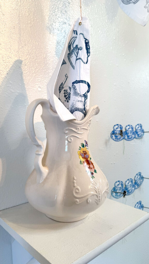 installation with installation with silkscreen napkins attached to ceiling in an arch travelling from a box to a pitcher